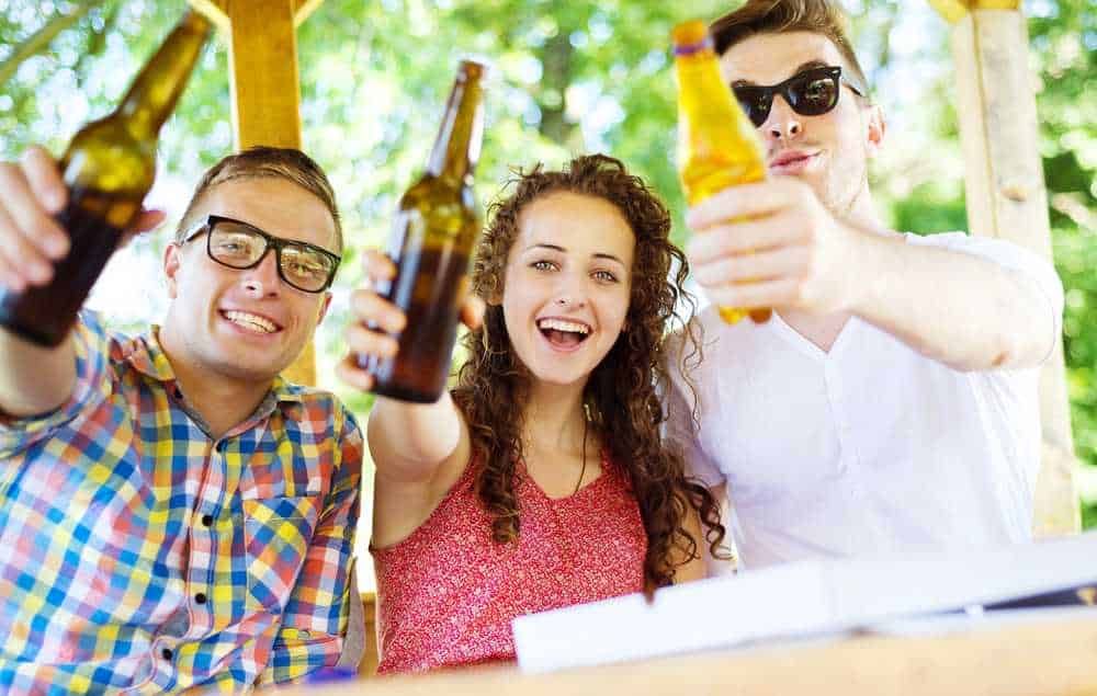 Birre artigianali con amici che sorridono e brindano all'aperto, festa estiva, allegria, convivialità, socializzazione, tema di divertimento in natura.
