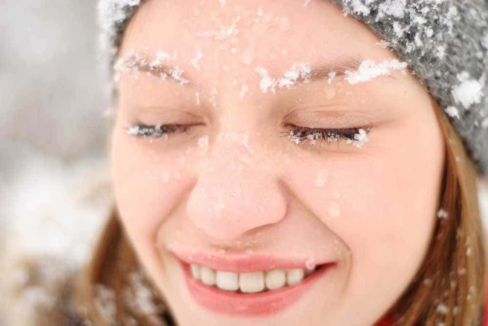 Nevicata su volto di ragazza sorridente con neve sui capelli, scena invernale, bellezza naturale, foto di inverno, gioia e serenità in un clima freddo.
