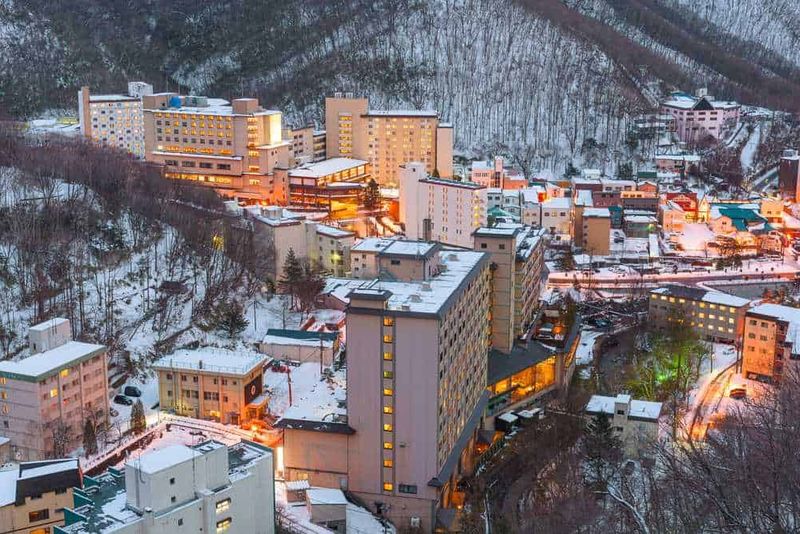 Tour Japan Golden Route in 10 giorni 6 Grattacieli sulla collina innevata di notte a frontale, vista aerea di un hotel di montagna in inverno illuminato, paesaggio urbano sulla neve, luci calde che riscaldano l'ambiente, struttura ricettiva isolata in montagna, cielo sereno e neve fresca, scenario di vacanza invernale.