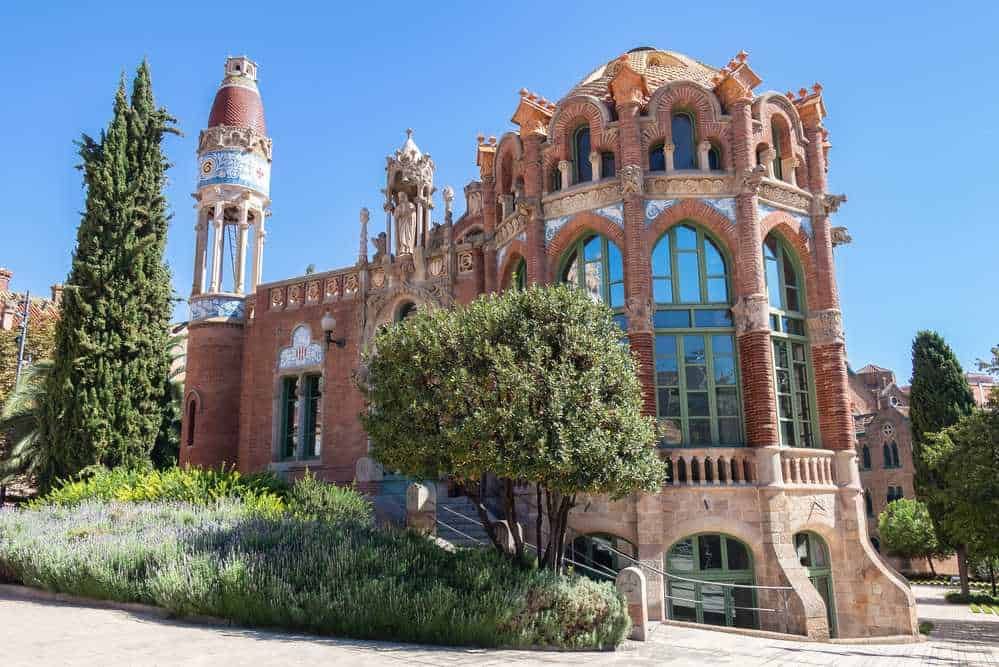 Villa de estilo architecture modernista con dettagli ornamentali, mattoni rossi e grandi finestrature in un parco verdeggiante, esempio di architettura innovativa in un ambiente naturale.