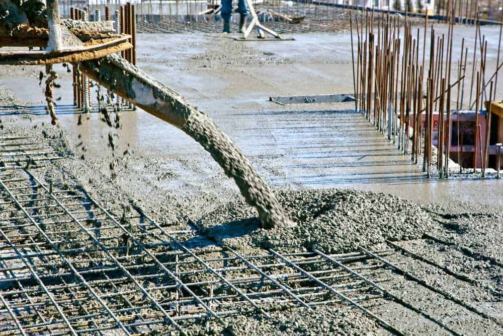 Versamento di calcestruzzo per rinforzo strutturale in cantiere edilizio. Lavori di costruzione con fondamenta in corso; ferro di armatura e superficie in cemento visibili.