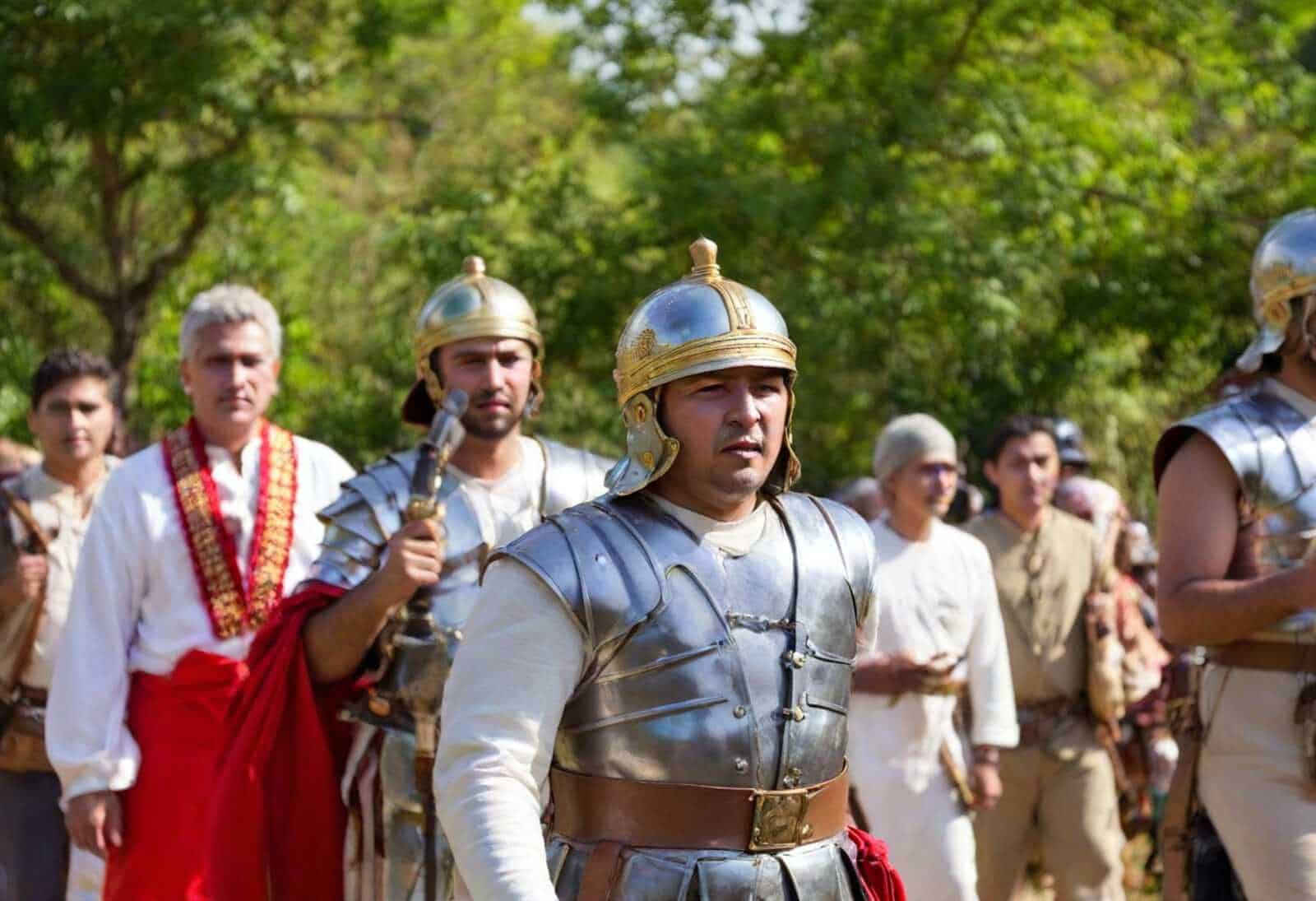 Guerrieri romani in costume storico durante rievocazione storica all'aperto, in un parco con alberi verdi.