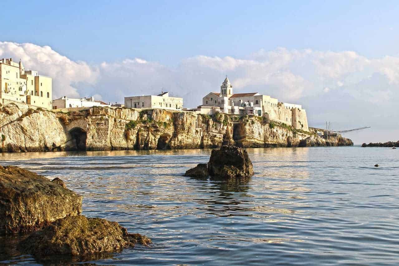 Fronte del mare con case bianche e scogli a Polignano a Mare, Puglia, Italia. Spiaggia naturale e vista panoramica sulla costa mediterranea. Paesaggio marino e architettura tradizionale pugliese.