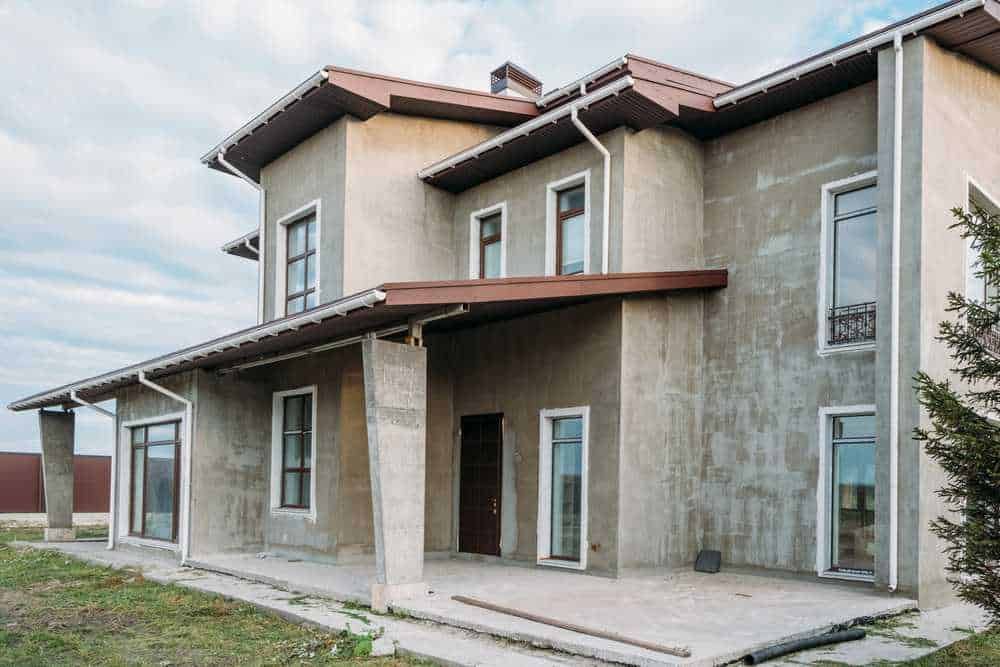 Casa in costruzione con struttura in cemento e finestre alte, pronta per lavori di finitura, immersa in un contesto di open space e natura, ideale per personalizzazione e abitare.