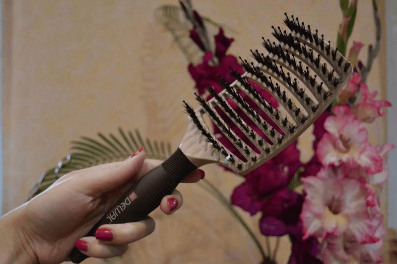 Quale pettine è migliore per i capelli? 10 Pettine per capelli con denti robusti in plastica e cuscinetti in gomma, utilizzato per acconciature e cura dei capelli, con sfondo di fiori rosa e tropicali, ideale per tutorial di hairstyling.