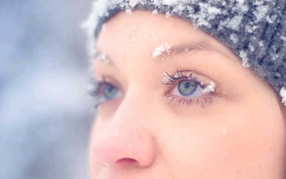 Neve sulla fronte, viso della donna, ritratto di una ragazza con cappello di lana in inverno, dettagli dei lineamenti e della pelle pure, atmosfera fredda e serena.