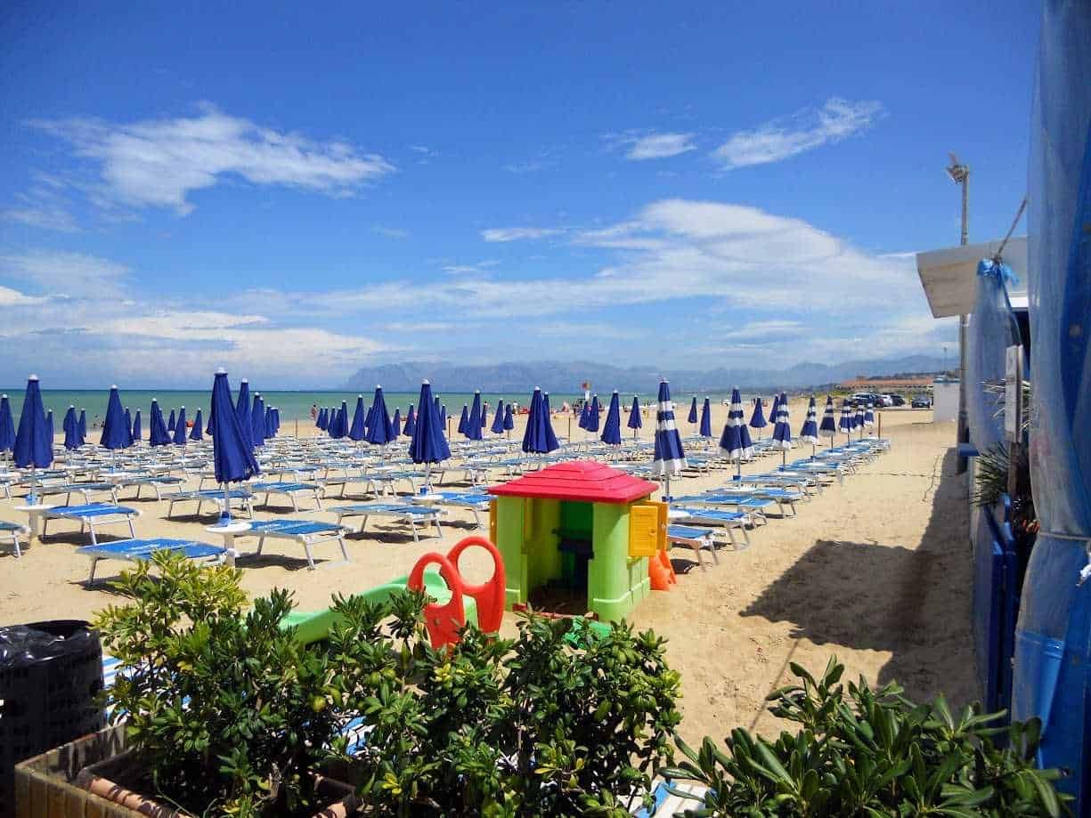 Sedia a sdraio con ombrelloni blu sulla spiaggia di Lignano Sabbiadoro, in Italia, con cielo sereno e mare calmo, ideale per relax e vacanze estive.