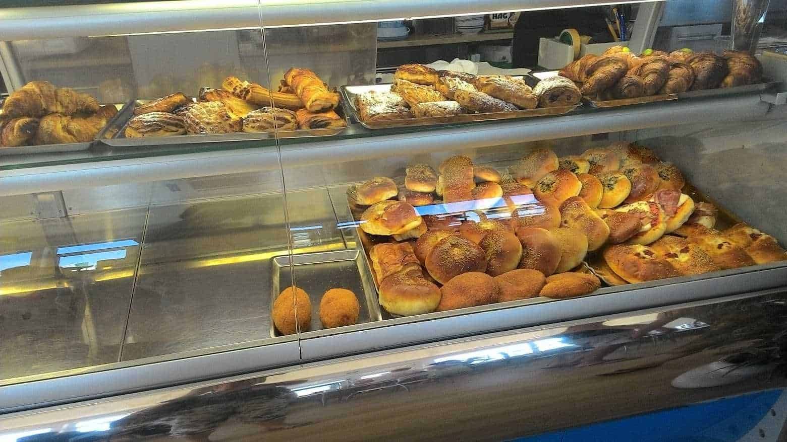 Pane assortito in una vetrina di pasticceria, inclusi bomboloni, croissant e focacce, ideale per colazioni e snack dolci e salati. Dagli impasti fragranti e rinomati per qualità e freschezza.