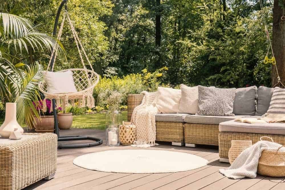 Relaxing outdoor patio with wicker furniture, hammock swing, lush greenery, and cozy cushions, perfect for outdoor leisure and enjoying nature.