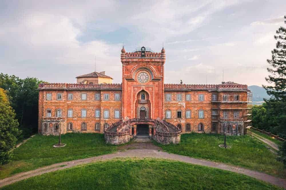 Castello in stile storico in pietra rossa, immerso nel verde con vista panoramica e dettagli architettonici eleganti, perfetto esempio di patrimonio culturale italiano.