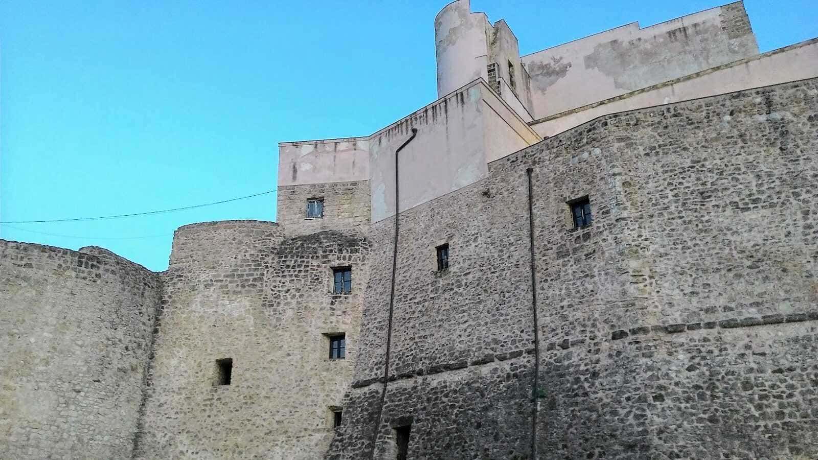 Antico castello in pietra con mura robuste e torrette, suggestivo esempio di architettura medievale immerso nel cielo azzurro.