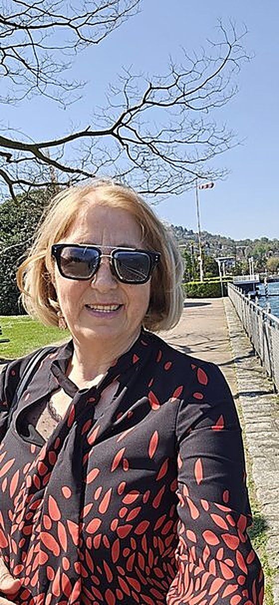 È tempo di arredare il giardino per la bella stagione 5 Donna sorridente con occhiali da sole, in abbigliamento elegante, in un parco vicino al lago con alberi e cielo azzurro, perfetta per l'arredamento esterno primaverile.