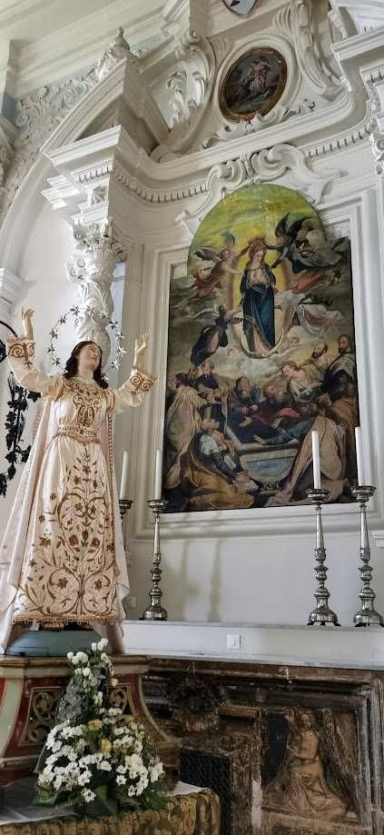 Cosa vedere a Guardiagrele e dintorni Abruzzo 13 Immagine di una chiesa barocca con un altare ornate e un dipinto religioso di grande formato sulla parete. Cassettone con fiori e statua di una Madonna con le braccia aperte di fronte all'altare, in un ambiente ricco di dettagli decorativi classici.