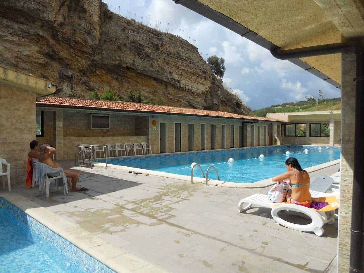 Piscina all'aperto con vista su scogliera e donne che si rilassano sotto il sole.