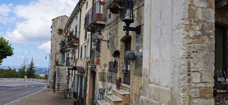 Cosa vedere a Guardiagrele e dintorni Abruzzo 11 Vecchio edificio in pietra con oggetti d'epoca e piante sui balconi, stradina di paese in stile rustico, atmosfera suggestiva, presenza di lampioni e decorazioni vintage, esempio di architettura tradizionale italiana.