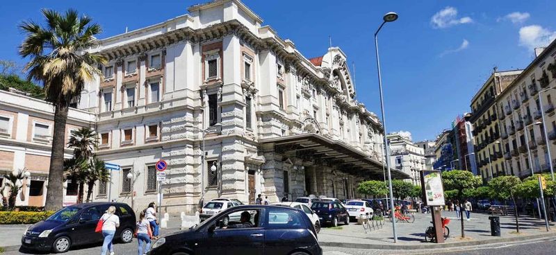 Stazione treni Mergellina a Napoli 6 Palazzo storico sulla strada principale di Napoli, con architettura elegante e dettagli decorativi. Strada trafficata con auto, bici e pedoni sotto un cielo azzurro.