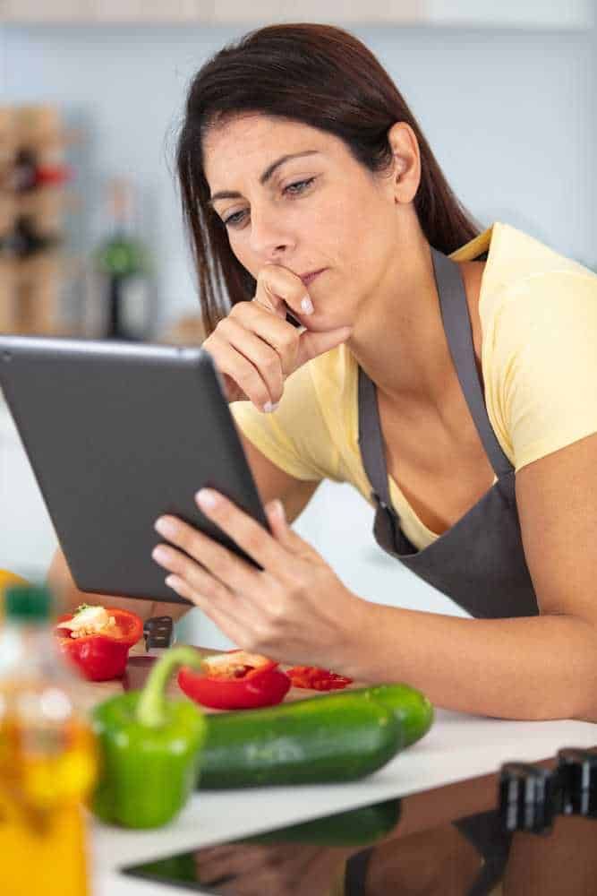 Può leggere ricette sul tablet in cucina con verdure fresche e pomodori freschi sul tavolo, concentrarsi sulla cucina e sulla tecnologia in un ambiente domestico.