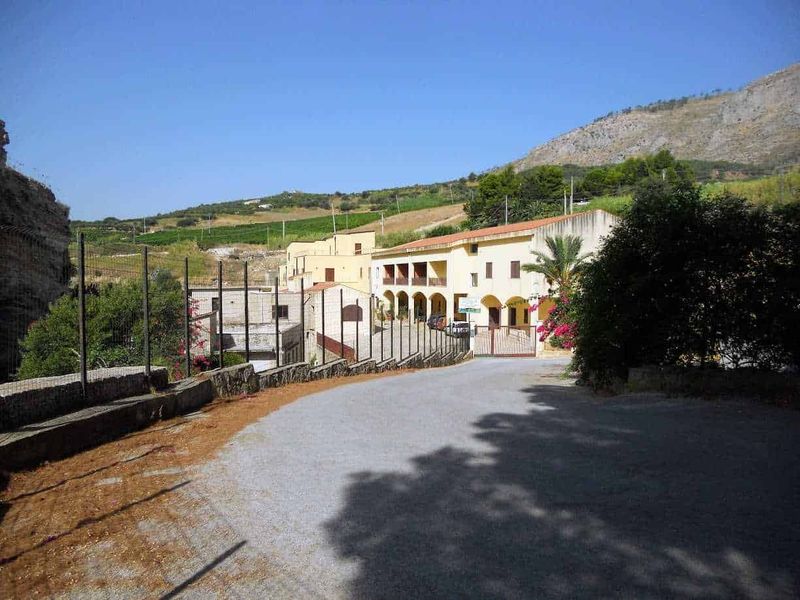 Castellammare del Golfo attrazioni e dintorni 8 Magazzino storico in stile mediterraneo con archi e balconi, immerso in una pittoresca campagna collinare, circondato da natura e vigneti, ideale per blog di viaggi e lifestyle.