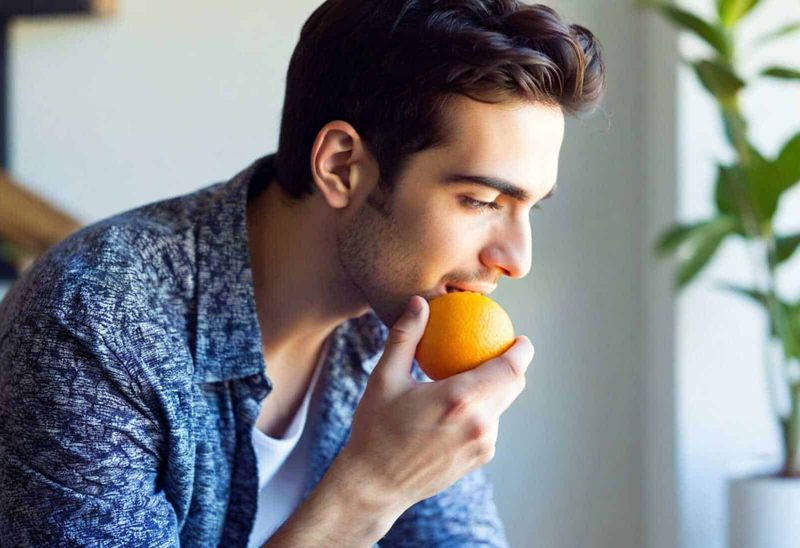 Benefici della vitamina C per la pelle 5 Arancia fresca mangiata da un giovane uomo, concetto di alimentazione sana e frutta naturale.