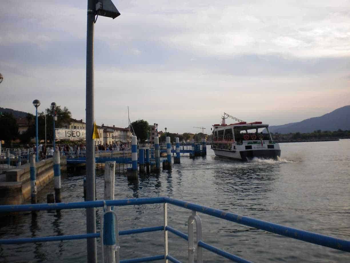 Porto turistico di Iseo con barca che si imbarca sul lago, atmosfera serale e paesaggio montano sullo sfondo, ideale per immagini di viaggi e viaggi in barca.