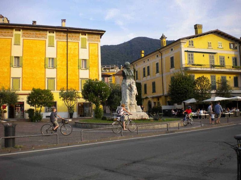 Cosa Vedere a Iseo città sul Lago di Iseo: centro storico, castello e lungolago 6 Busto storico nel centro di Iseo, Piazza Garibaldi, una città italiana con edifici colorati, bambini in bicicletta e gente che passeggia, con montagne sullo sfondo, atmosfera vivace e rilassante.