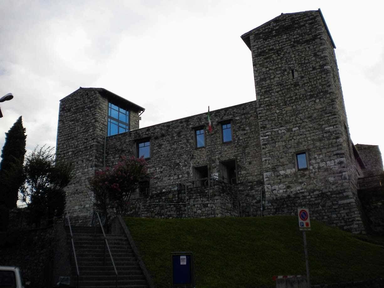 Castello Oldofredi, medievale in pietra con torri, situato su una collina, con bandiera italiana, palazzi storici, vista panoramica, in Italia, esempio di architettura storica e patrimonio culturale.
