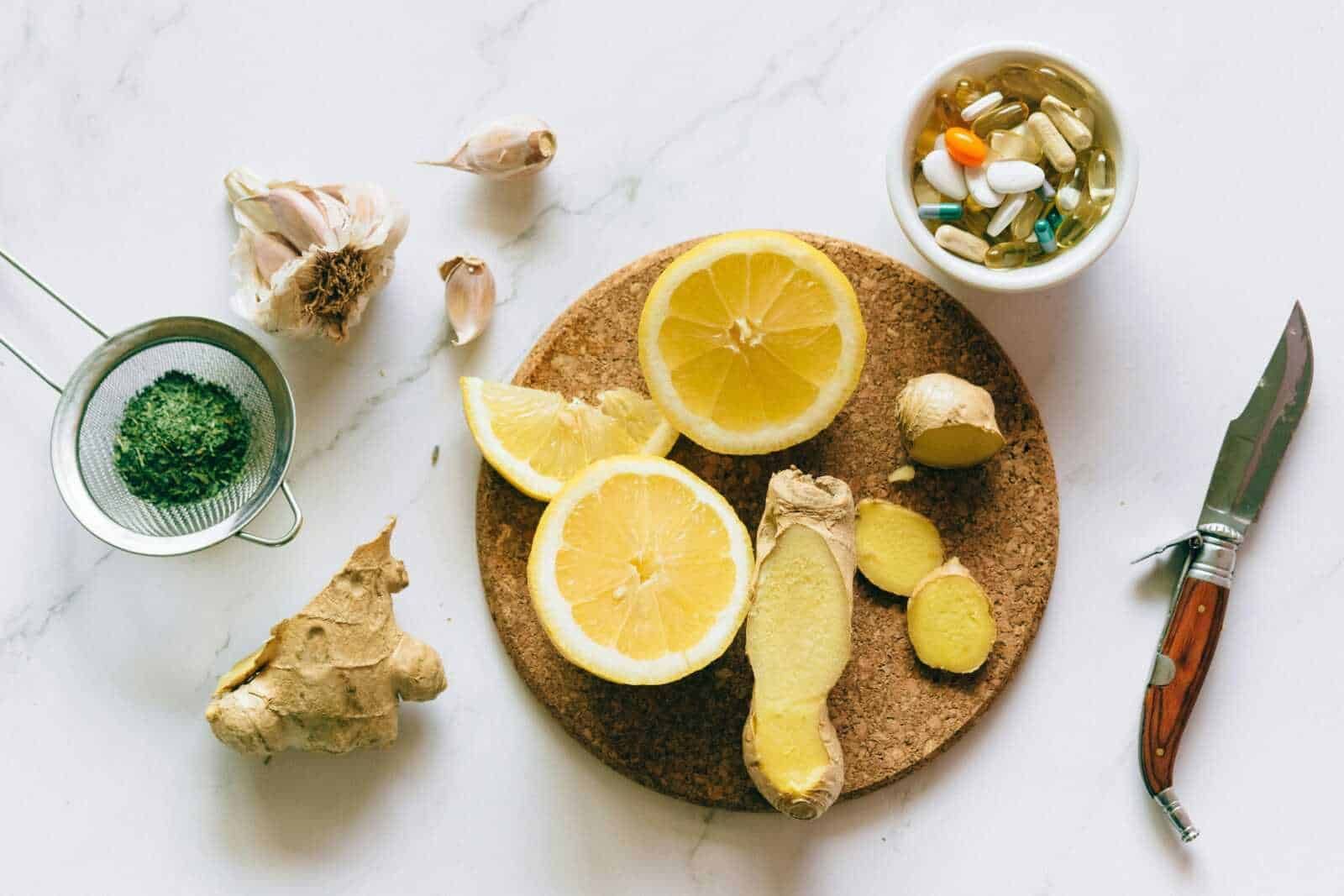 Limone fresco, zenzero e spezie in capsule su un tavolo bianco; ingredienti naturali per rimedi e integratori, con coltello e erbe aromatiche.