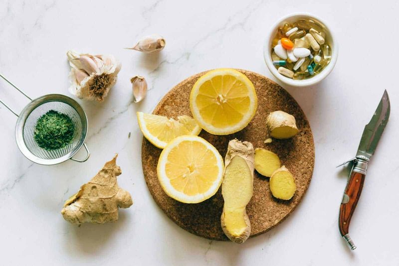 8 Rimedi naturali con lo zenzero: benefici, proprietà e come usarlo 3 Limone fresco, zenzero e spezie in capsule su un tavolo bianco; ingredienti naturali per rimedi e integratori, con coltello e erbe aromatiche.