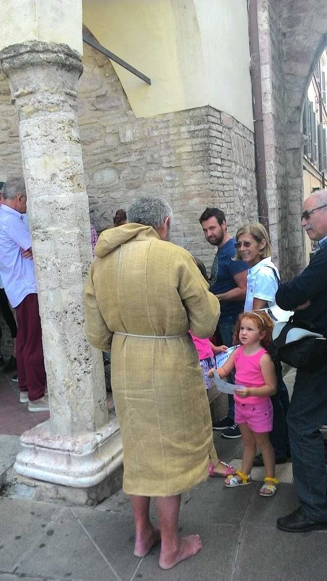 Assisi cosa vedere: itinerario tra arte e patrimonio UNESCO (2026) 14 Piazza storica di Assisi con persone che chiacchierano vicino a colonne in pietra e mura antiche