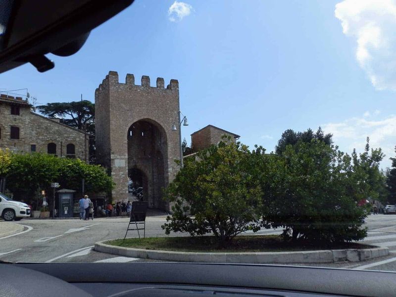 Assisi cosa vedere: itinerario tra arte e patrimonio UNESCO (2026) 4 Antico arco Medievale in pietra situato nel centro storico di Assisi, un paese italiano, con persone che passeggiano e auto parcheggiate