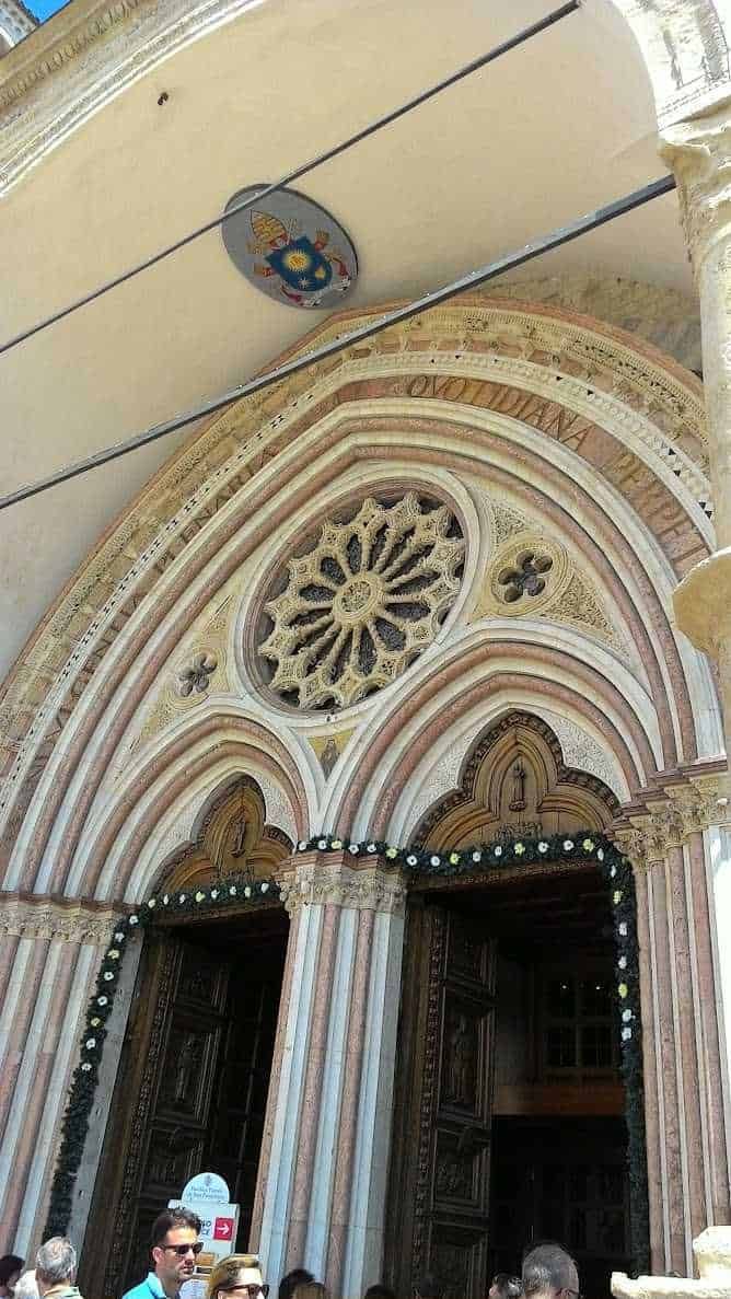 Assisi cosa vedere: itinerario tra arte e patrimonio UNESCO (2026) 7 Ingresso della facciata della Basilica di San Francesco ad Assisi con dettagli architettonici in stile gotico, archi decorativi e rose in pietra.