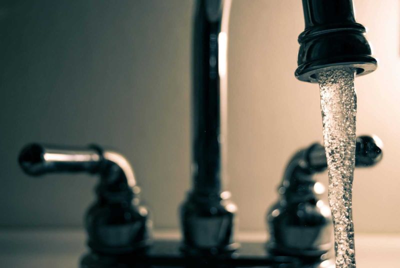 Acqua pura, salute sicura: perché scegliere un depuratore d'acqua per la tua casa 3 Rubinetto dell'acqua aperto con gocciolamento, dettaglio di un lavabo domestico, immagine simbolo di FAQ, problemi idraulici e manutenzione domestica.