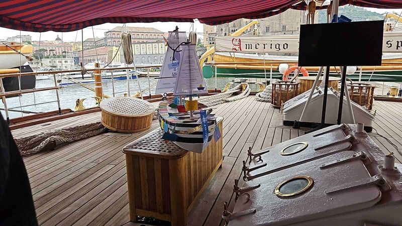 Amerigo Vespucci a Napoli 2025: cosa sapere 6 Sedia e arredamento su una barca a vela con vista sul porto e sulle barche circostanti.