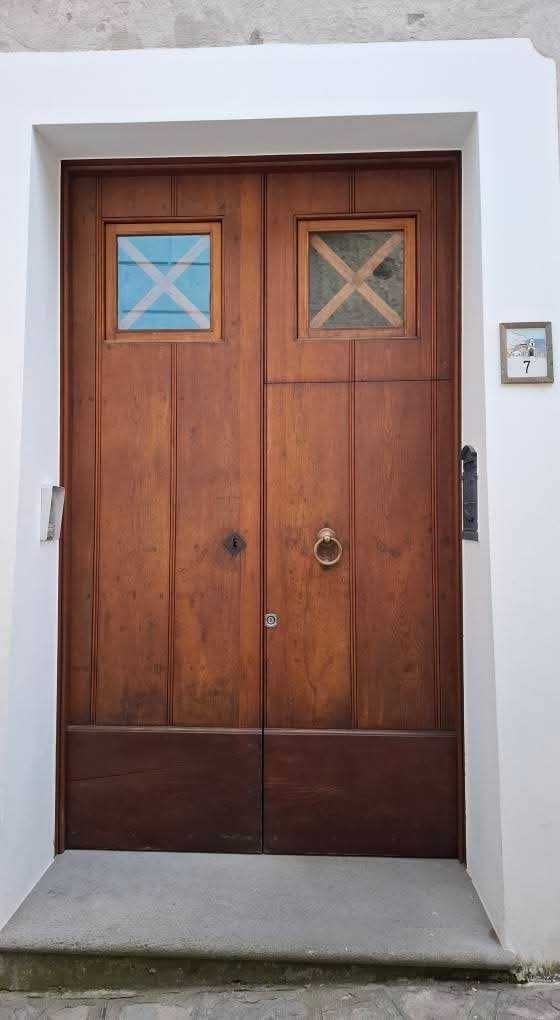 Elegante porta in legno massello con dettagli nella parte superiore e maniglione in ottone, ideale per l'ingresso di una casa moderna o tradizionale.