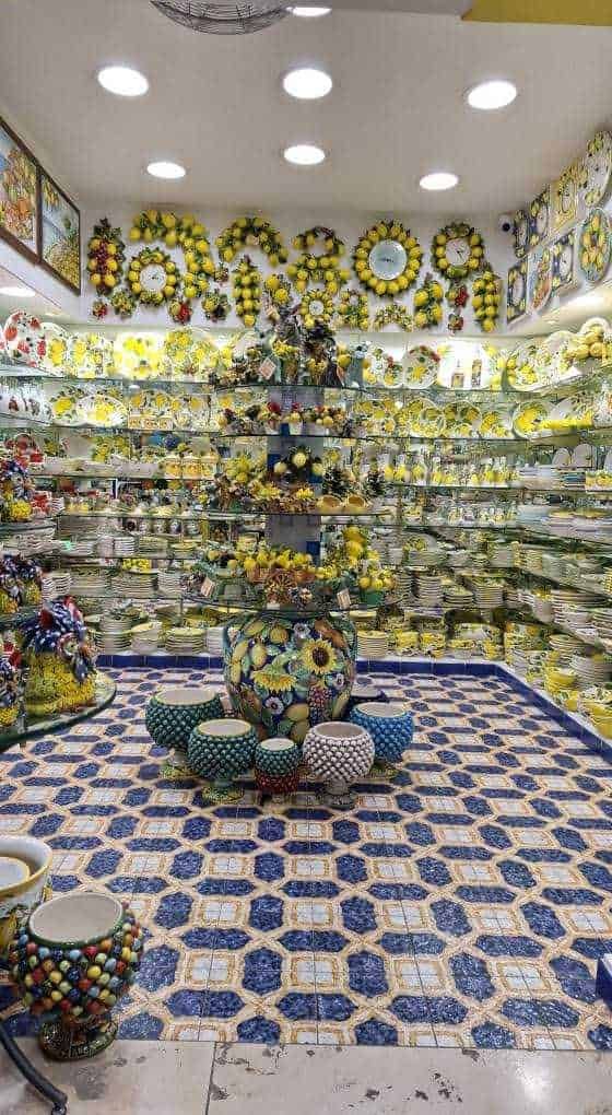 Vaso decorato con girasoli e decorazioni floreali gialle, esposizione di piatti e oggetti in ceramica in stile estivo e colorato.