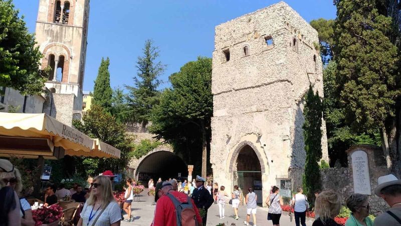 Stili dei portoni a Ravello: dal Medioevo al rustico 11 Antico torre e chiesa storica a Ravello con turisti e sfondo cielo blu, famosa attrazione culturale e storica in Italia.