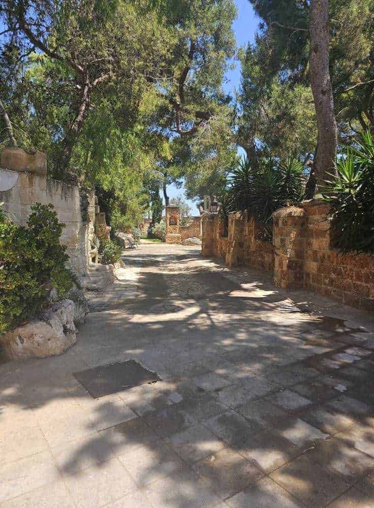 Antico vicolo di pietra con muri in stile mediterraneo e alberi ombreggianti, atmosfera tranquilla e rilassante, perfetta per appunti sul blog di viaggi e storia.