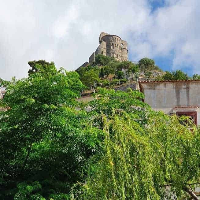 Torre medievale su collina verdeggiante con vegetazione rigogliosa e cielo nuvoloso, vista panoramica su un paesaggio storico e naturale in Italia.