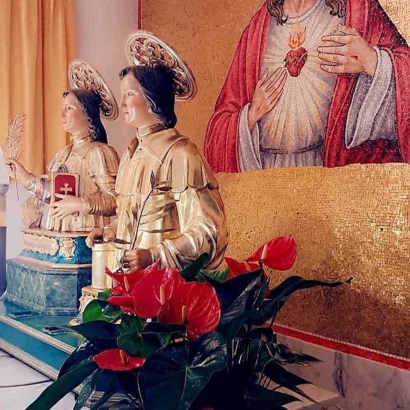 Chiesa San Cosimo e Damiano Ravello, Italia 3 Statuette religiose raffiguranti santi con dettagli dorati, decorazioni natalizie con piante verdi e fiori rossi, in ambiente sacro con mosaici dorati e iconografia religiosa.