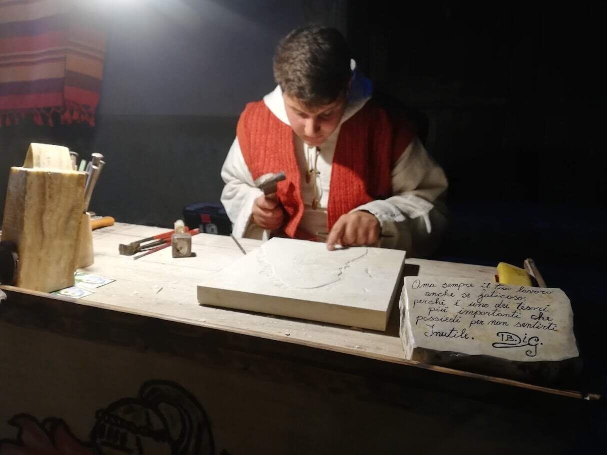 Piastra da lavoro per sculture in marmo con artista al lavoro, strumenti artigianali e appunti sul lavoro, ambientazione di un laboratorio artistico italiano.