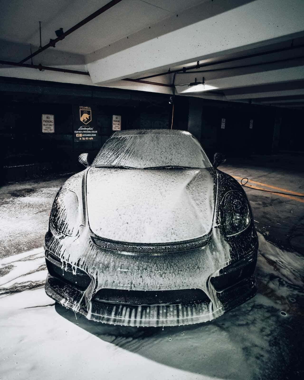 Pulizia auto Lamborghini con schiuma nel parcheggio sotterraneo, cura e manutenzione del veicolo di lusso, dettagli estetici e servizio professionale.