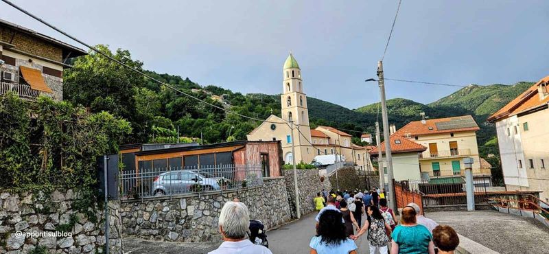 Agerola fior di latte, porta della Divina Costiera 5 Cammino di turisti in un pittoresco villaggio italiano con chiesa storica, tra case con tetti in terracotta e paesaggi montani rigogliosi, perfetto per fotografie di viaggio, cultura e turismo in Italia.