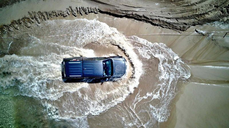 Come guidare correttamente nelle aree allagate 3 Auto 4x4 che attraversa un'enorme pozzanghera di fango e acqua, sfiorando le pareti di un canyon naturale, in un'avventura off-road in un paesaggio selvaggio e accidentato.