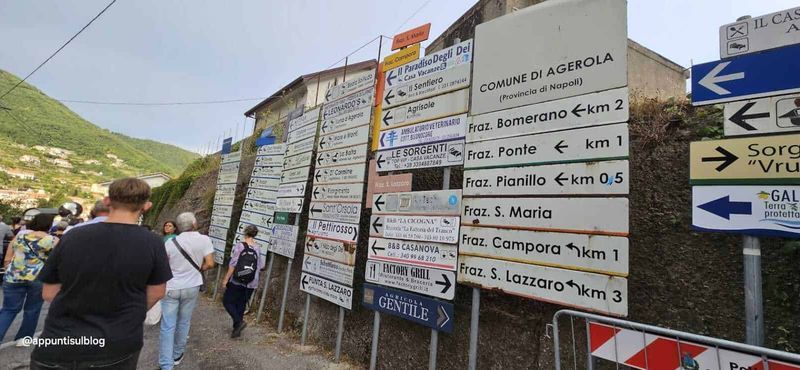 Agerola fior di latte, porta della Divina Costiera 3 Segnali stradali con indicazioni di località e frazioni a Agerola, Italia, in un paesaggio montano. Persone che camminano lungo una strada di montagna; cartelli turistici e di indicazioni stradali.