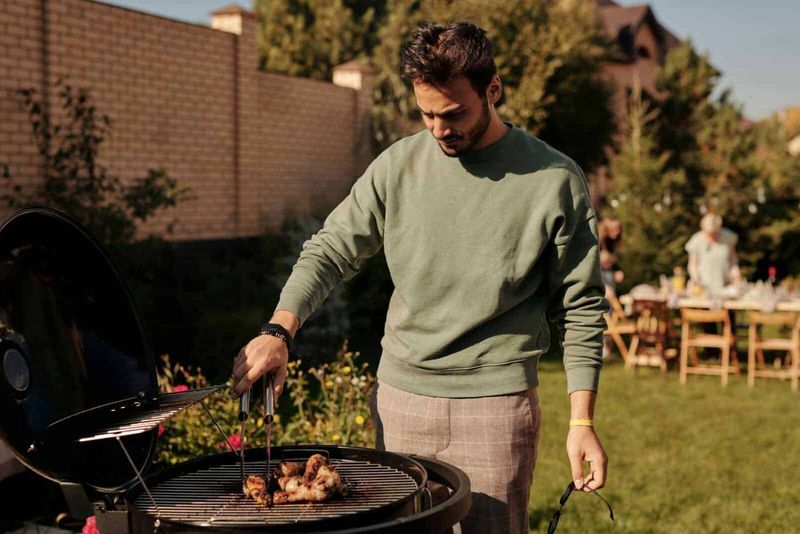 Ferragosto come si festeggia in Italia 2 Ferragosto in italia: Grigliata all'aperto in giardino durante un barbecue estivo, con un uomo che controlla le carne sulla griglia, atmosfera conviviale e momenti di relax all'aperto.