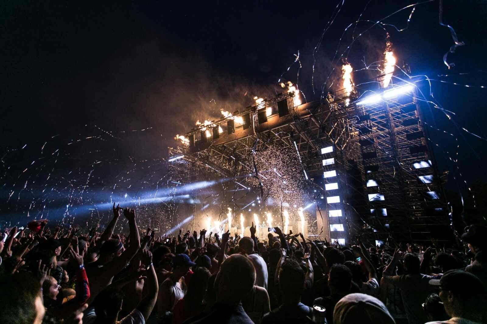 Festa di musica dal vivo con fuochi d'artificio, luci e pubblico entusiasta che si diverte a un concerto notturno, atmosfera di festa e emozione vibrante.