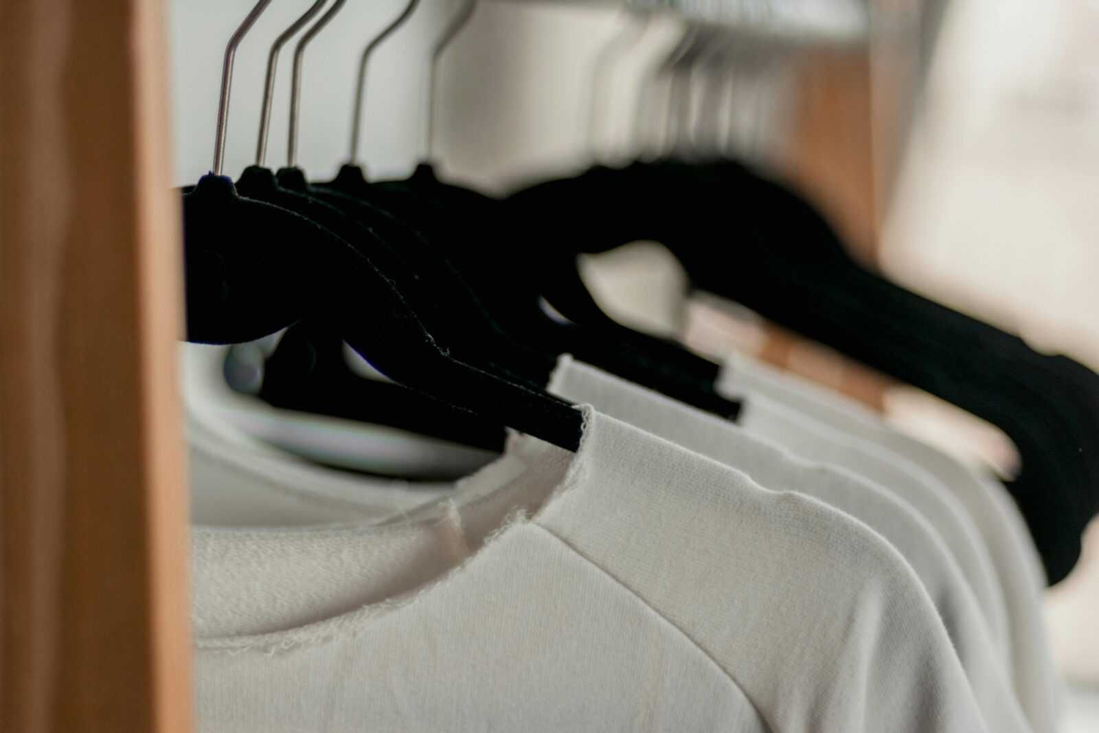 Vestiti su appendiabiti nel guardaroba, abbigliamento casual, magliette e felpe in bianco e nero, organizzazione wardrobe, stile minimalista.