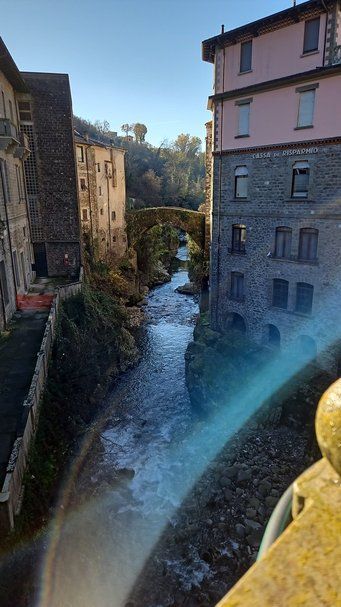 Vecchio ponte sul fiume tra edifici storici in un paesaggio urbano, con luce naturale e cielo blu, rappresenta un angolo pittoresco di un borgo italiano.