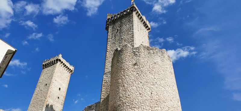 Come si riconoscono le case-torri medievali 6 Torri medievali in pietra in un paesaggio urbano italiano, simbolo di storia e architettura antica, con cielo azzurro e nuvole bianche sullo sfondo.