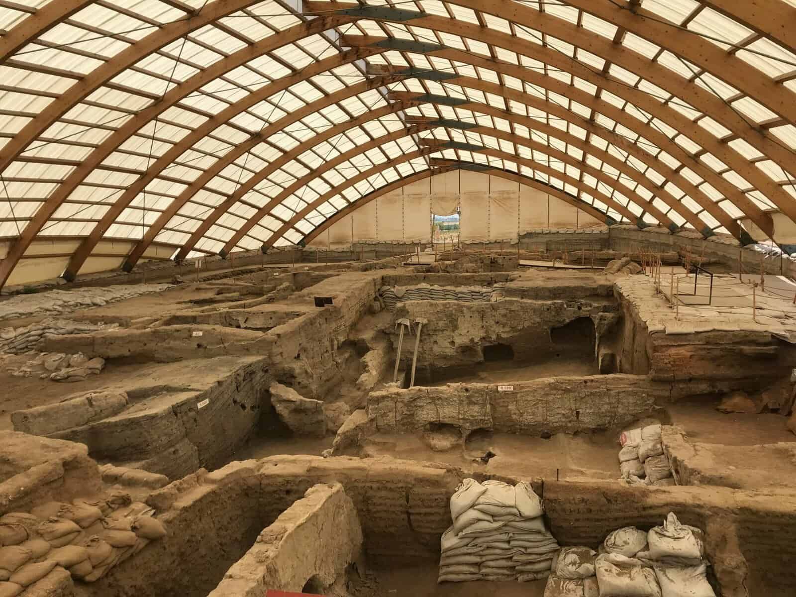 Antico sito archeologico con scavi e resti di strutture romane, custodito sotto una struttura moderna in vetro e legno, ideale per appunti su blog di storia, archeologia e scoperte storiche.